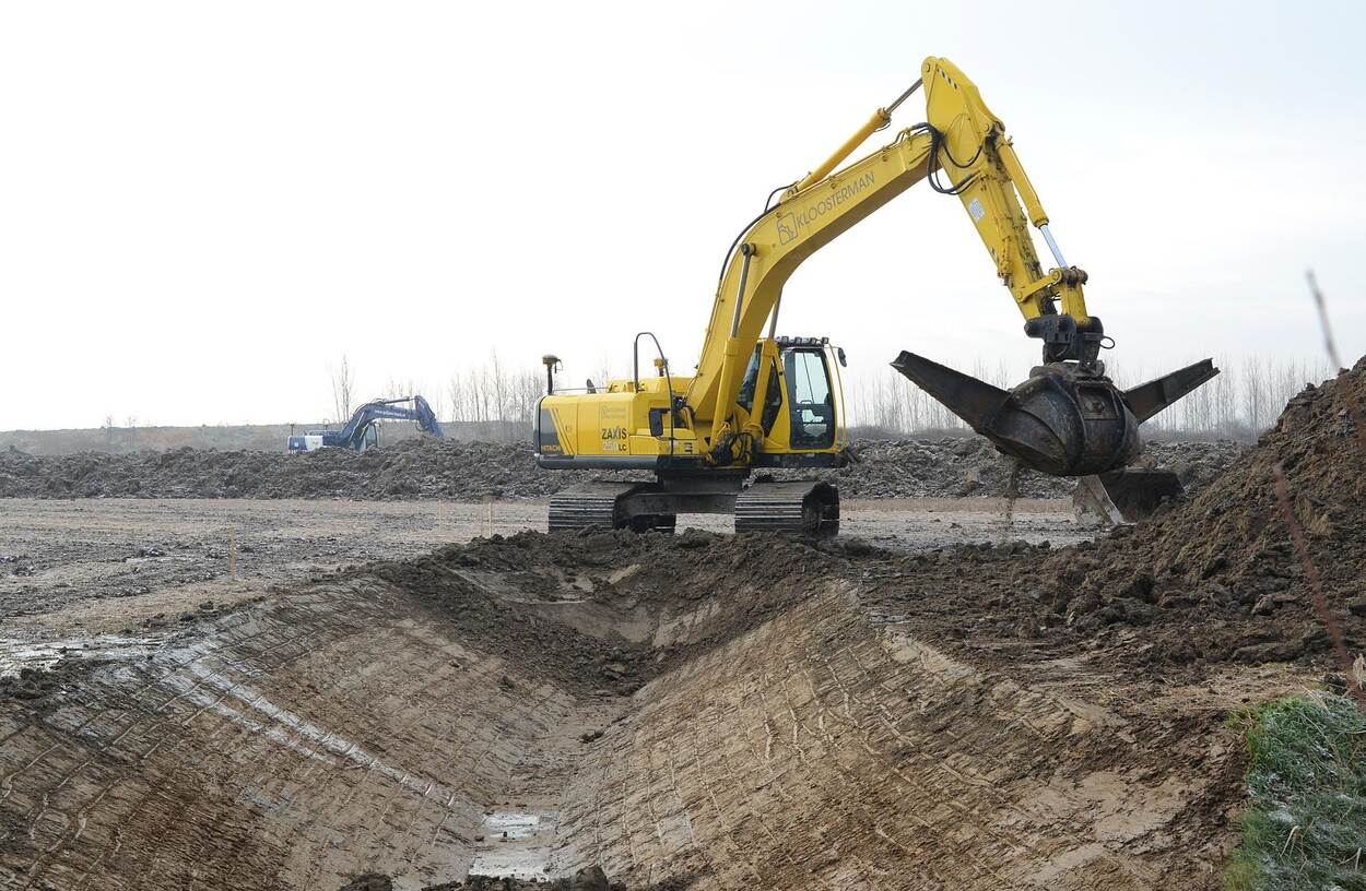 Een kraan met grijper graaft een sloot uit en gooit het uitgegraven zand op een hoop ernaast. Op de achtergrond is nog een kraan bezig.