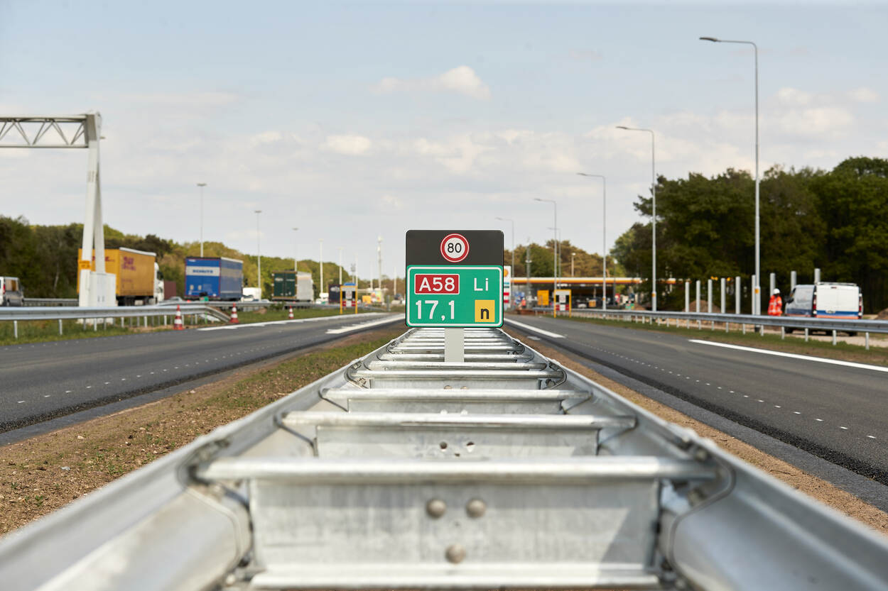 Een wegwijzerbord langs de A58 met de aanduiding "A58 Li 17,1" en een snelheidslimiet van 80 km/u. Op de achtergrond zijn vrachtwagens, een tankstation en verkeersborden zichtbaar.